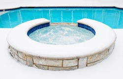 Outdoor hot tub or spa by swimming pool surrounded by snow in the winter