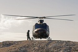 Pilot checking military helicopter before taking off from helipad on top of mountain. Military, airforce, defense and mountain rescue concepts.