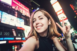 Young woman tourist laughing and taking selfie photo in New York City, Manhattan, Times Square. Female traveler and photographer takes picture for her blog.