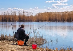 A fisherman with a fishing rod sitting on a chair on the river bank. The concept of a rural getaway. 