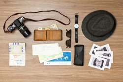 International travel background with a retro or vintage touch. Items include an old photo camera, passport, wallet with currency, airplane ticket, hat, sunglasses and black and white photos