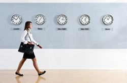 Business woman walking in a hurry past a row of clocks showing the time in various parts of the world. Business, travel, time concept