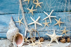 Maritime souvenir from holidays on the beach: Seashell background border on rustic blue wood. View on different starships and seashells with white sand and fishnet.