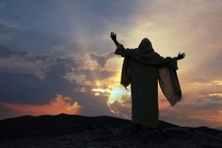 Jesus praying alone with raised hands on a hill at sunset. Biblical concept.