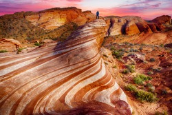 Unrecognizable hiker is watching spectacular sunset from the Wave rock in Valley of Fire State Park, Nevada, USA