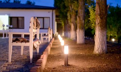 Row of Illuminated Outdoor Lights in Ground Alongside Stone Patio Furnished with Wooden Benches and Plaid Blankets Creating a Cozy and Inviting Atmosphere