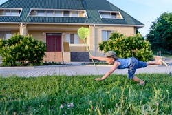 Little boy having fun catching insects crouching down on the lush green lawn outside a house with a net in his hand