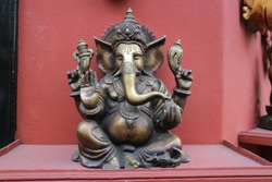Bronze statuette of the Hindu god Ganesha on the background of a red wall.