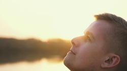 Close up portrait of pensive handsome young man looking up enjoying nature in sun rays at sunset. slow motion.