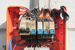 Burning switchboard from overload or short circuit on wall. Circuit breakers on fire and smoke from overheating due to poor connection. Dangerous home electrical wiring concept, closeup view