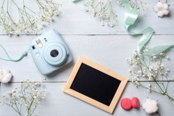 Modern polaroid camera, macaroon cookies, photo frame, flowers on rustic blue wooden background. Top view, tender minimal flat lay style composition. Womens desk, fashion blogger, beauty technology
