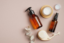Bathroom cosmetics and accessories on brown background. Flat lay, top view. Pump bottle, cosmetic spray lotion, candles, body clean brush, eucalyptus leaf.