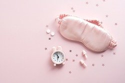 Female eye mask, alarm clock, earplugs, pills on pink background with confetti. Insomnia treatment concept.