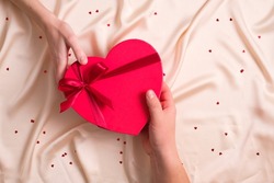 Man's hand gives red heart-shaped gift to female hand. Happy Valentines Day, Happy Birthday concept.