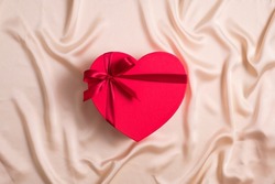 Red heart-shaped box wrapped ribbon now on silk background. Happy Valentines Day concept. Flat lay, top view.