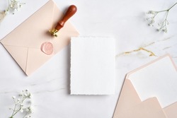 Wedding stationery set on marble desk top view. Blank paper card mockup, pastel pink envelopes with wax seal stamp, gypsophila flowers.