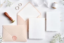 Wedding stationery set. Flat lay wedding invitations, pastel pink envelopes, wax seal stamp, golden rings, flowers on marble desk. 