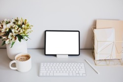 Digital tablet mockup with pen, keyboard, cup of coffee, paper notebooks, flowers on home office desk table. Stylish feminine workspace. Minimal style.