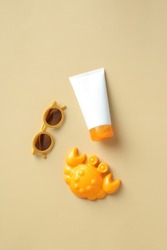 Flat lay sunscreen lotion tube, kids sunglasses and crab sandbox toy on beige table. Infant skin care, sun protection concept.