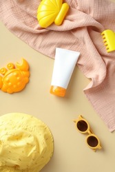 Sun protection cream tube for babies and children with panama hat, towel, sunglasses, sandbox toys on beige background. Sunscreen lotion for kids. Flat lay, top view.