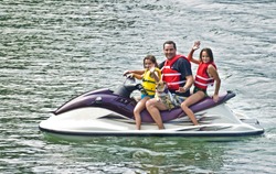A man with his girls and dog waving from a jet ski.