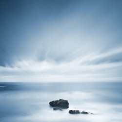 Dark rocks in a blue ocean under cloudy sky in a bad weather. Long exposure photography