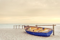 Tropical Seascape with a wooden, old and broken yellow blue boat on white beach on warm sunset.