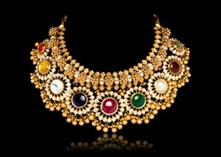 A beautiful golden necklace with multi colored gem stones on dark black background.