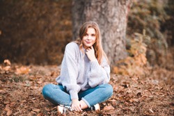 Beautiful teen girl 14-15 year old wearing stylish clothes sitting outdoors. Looking at camera. Autumn season. 