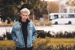 Young serious teen boy 15-16 year old wearing denim jacket and hoodie posing over city street background closeup. Looking at camera. Teenagerhood. 