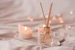 Home aroma fragrance diffuser with burning candles on white tray in bed over glowing lights close up. Cozy atmosphere. Wellness. Healthy lifestyle. 
