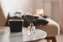 Bamboo sticks in bottle with scented candles and cup of tea on marble table closeup. Home aroma. Aromatherapy. Apartment living. 