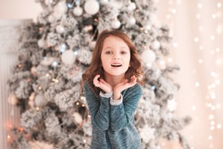 Happy kid girl 4-5 year old laughing in room over christmas tree. Wearing stylish knitted sweater. Looking at camera. Childhood. Christmas time. 