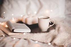 Open book with cup of tea in bed at night close up. Cozy atmosphere. 