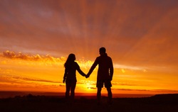 Loving couple stands against the backdrop of a beautiful fiery sunset. The sun's rays shine through the clouds. Romantic atmosphere.