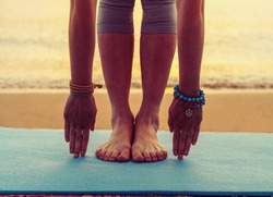 Young woman doing yoga exercise on beach near the sea at sunset in summer, face is not visible