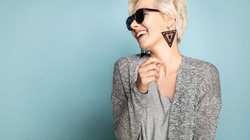 Waist up portrait of happy joyful blonde in stylish casual clothes. Engaging lovely female with short fair hair in sunglasses. Isolated on blue background