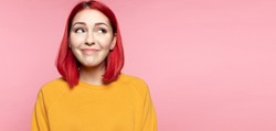 Modern young pink haired shy girl looking aside, feeling embarrassed. Smiling bashful confused caucasian female dreaming imagining idea on pink studio background. Human emotions, modest person concept