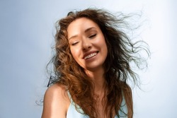 Portrait of happy young woman smiling in the sunshine on  blue background. Model with curly  hair and perfect skin. Haircare concept.