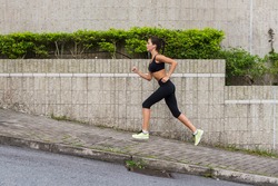 Slim young woman running uphill on sidewalk of city street. Female athlete training outside