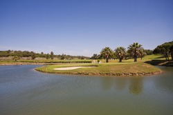 A nice view of a golf course with a lake and blue sky.