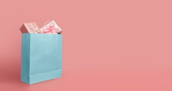 Gift boxes in blue paper shopping bag on isolated pink background with copy space. Black Friday, Sales, Giving Gift for Christmas and New Year 2019.