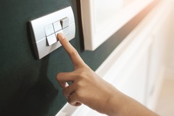 Closeup of Asian female right hand is turning on or off on grey light switch over green wall. Copy space.