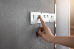 Asian female right hand is turning on or off on grey light switch over gray textile texture wall at the house or hotel. Copy space.