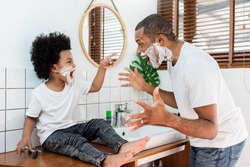 Black African American Man and little son laughing playing shaving foam in bathroom together.