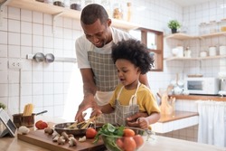 Black African American Father teaching his Afro son cooking in kitchen at home