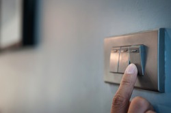 Close up male hand or fingers turn on or off on grey light switch with dark blue wall in the night time at home. Power, Energy, Safety, Saving Electrical. Copy space. 