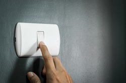 Male finger turn on or off white lighting switch on rough dark grey wall. Copy space.