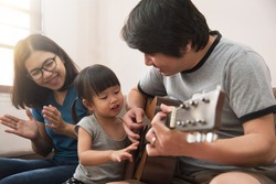 Happy family. Asian young father, mother and daughter playing the guitar together.