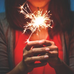 Happy Asian Woman in red shirt having fun while holding sparkler on blue background.